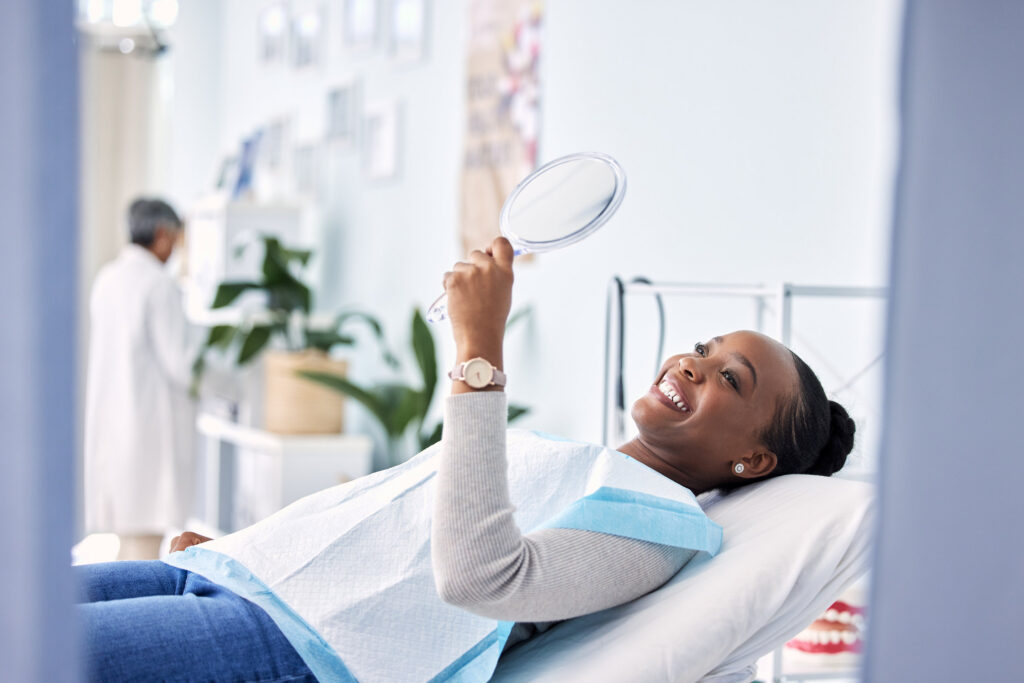 Smile, mirror and black woman at dentist on chair in clinic, tooth treatment and cleaning. Reflection, dental orthodontics and happy person teeth whitening, oral hygiene and healthcare for wellness.
